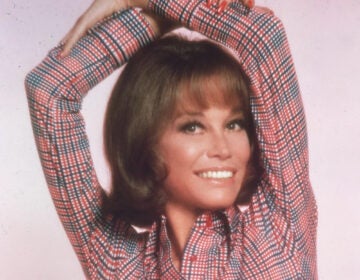A headshot of a young Mary Tyler Moore with her arms crossed above her head.