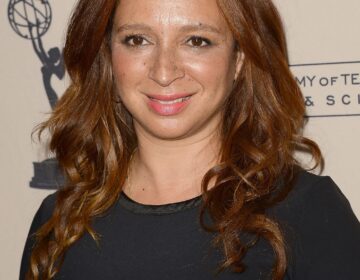 A headshot of Maya Rudolph on a red carpet wearing a black dress and smiling.