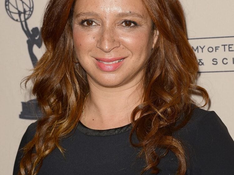 A headshot of Maya Rudolph on a red carpet wearing a black dress and smiling.