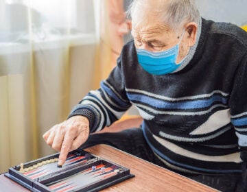 Senior man wearing a medical mask during COVID-19 coronavirus playing backgammon in a nursing home