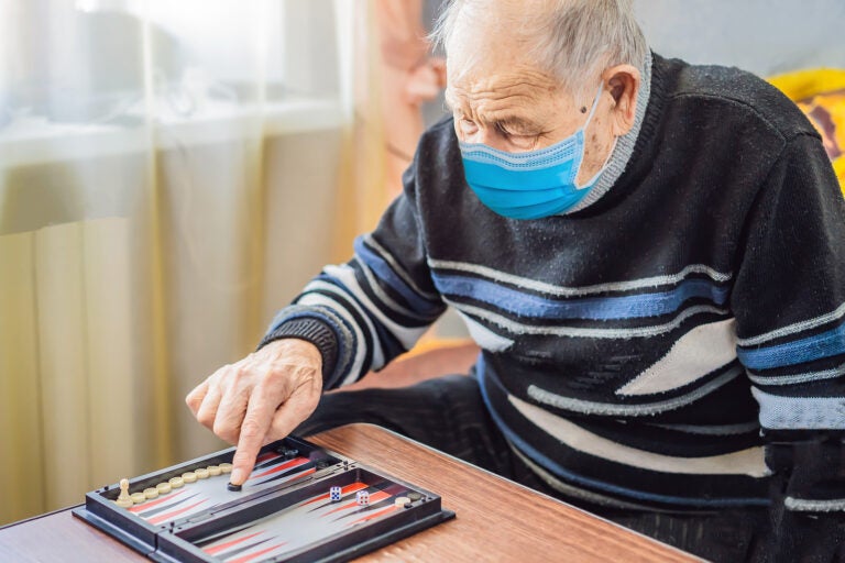 Senior man wearing a medical mask during COVID-19 coronavirus playing backgammon in a nursing home