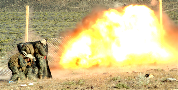  Marines from Combat Engineer Platoon, Marine Wing Support Squadron 473 blow a hole in a fence at Hawthorne Army Weapons Depot in Nevada on June 17, 2010 during demolitions training for exercise Javelin Thrust 2010. The Marines used a kevlar blanket to shield themselves from fragmentation and to reduce the impact of the blast. (Photo by Pfc. Nana Dannsaappiah) 