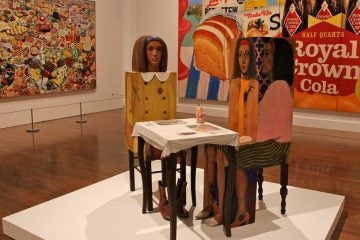 'Dinner Date,'  a sculpture by Marisol, is displayed against the backdrop of Icelandic artist Erro's 'Foodscape' (left) and Tom Wesselmann's 'Still Life #35.'. They are part of the Philadelphia Museum of Art's exhibit on the development of Pop Art. (Emma Lee/WHYY)