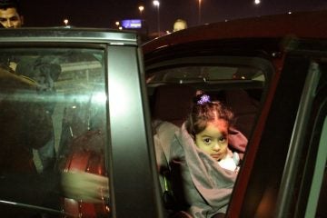 Three-year-old Noor Hasan is settled into a car seat in the cell phone lot at Philadelphia airport after her family's flight from Burma. (Emma Lee/WHYY)