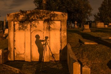 A photographer's shadow is cast against the wall of a mausoleum from the illumination of street lights. (Jonathan Wilson for Newsworks)