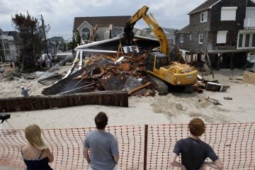 People watch from the beach Wednesday, July 10, 2013, as a home severely damaged by Superstorm Sandy is demolished in the Normandy Beach section of Toms River, N.J. (Mel Evans/AP Photo, file) 