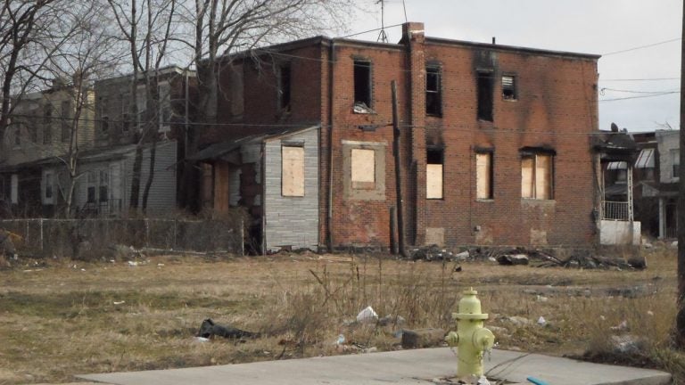 A house with boarded-up windows is visible on an empty lot on a winter's day.