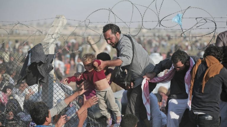  FILE - A Sunday, June 14, 2015 file photo of a Syrian refugee carrying a baby over the broken border fence into Turkey (AP Photo/Lefteris Pitarakis, File) 