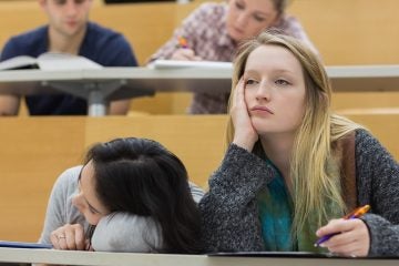 Demotivated students sitting in a lecture hall with one girl napping in college