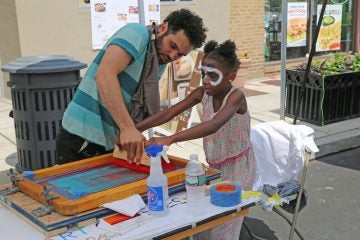 Jianni (L) and Manny Gonzales from Manayunk Roxborough Art Center pressing a custom printing on a T-shirt (Natavan Werbock/for NewsWorks)