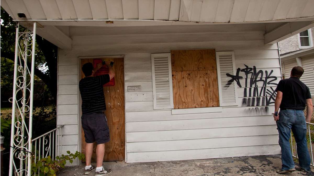  Developer Tom Moses (left) loosens boards blocking the entrance to a vacant home on Phil Ellena St. in Mt. Airy. (Brad Larrison/for NewsWorks) 