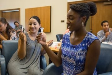 West Chester University seniors (from left) Arianna Sanchez, Alexa Stewart and Ashley Williams, swirl their saliva in collection tubes. The saliva is then mixed with a stablizing fluid and sent to the labs at Ancestry.com. (Emily Cohen/for NewsWorks)