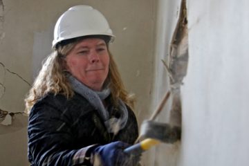 Pilar Hogan Closkey of St. Joseph's Carpenters Society swings a sledgehammer to start the interior demolition of a home on Harvard Avenue in Collingswood. (Emma Lee/WHYY)