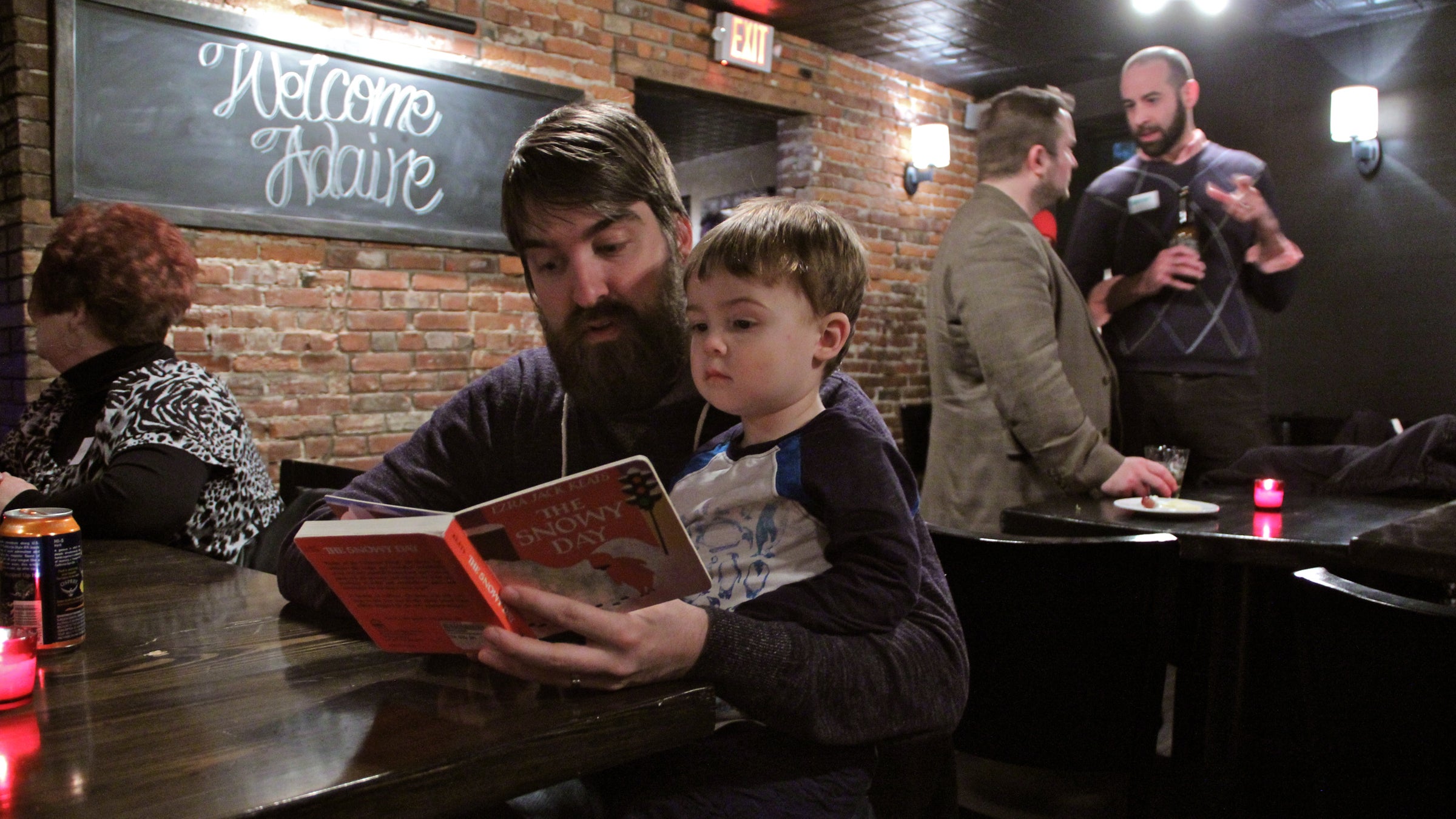  Joshua Park reads to his 2-year-old son, Jonah, during a fundraiser for Adaire Elementary School at Jerry's Bar in Fishtown. (Emma Lee/WHYY) 