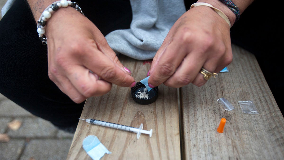 A woman prepares to shoot heroin in a public park. (Jessica Kourkounis/For Keystone Crossroads)