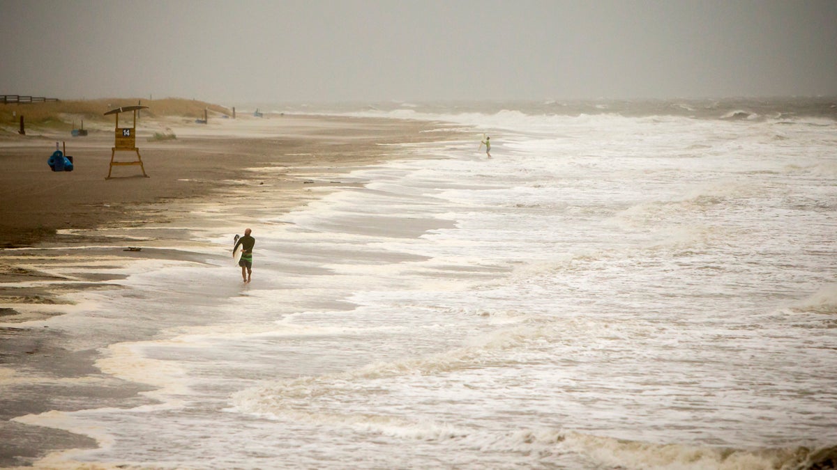 A surfer walks the beach while looking for waves from the surge of Hurricane Hermine