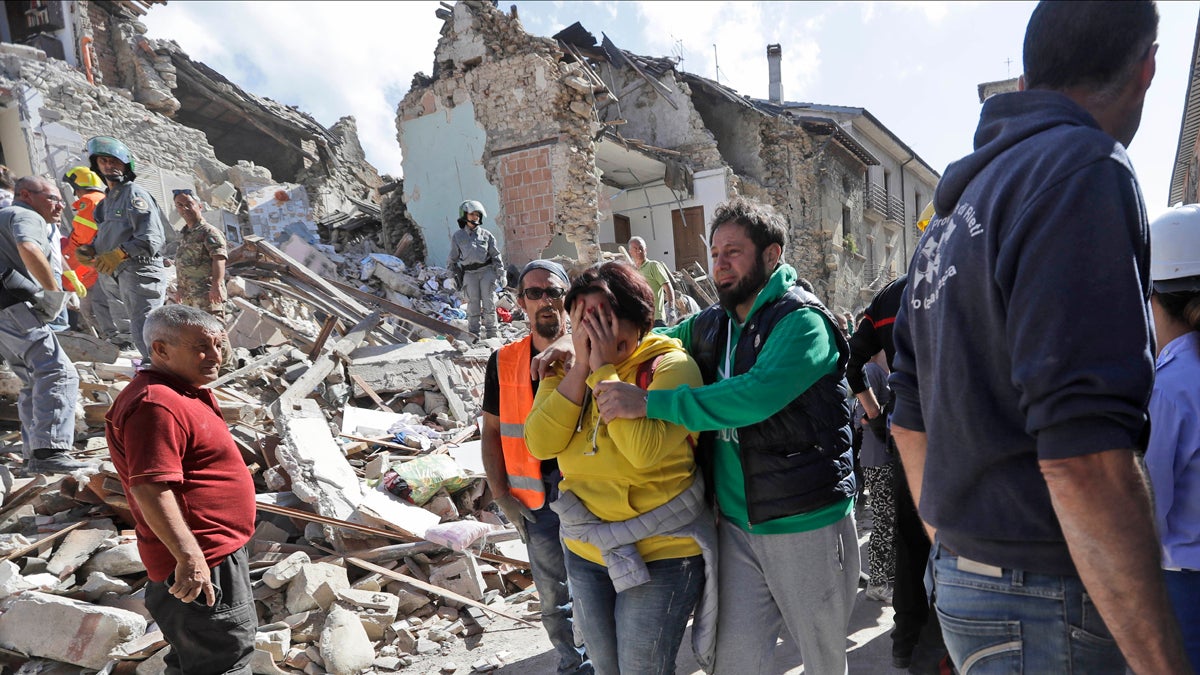 A woman is comforted as she walks through rubble after an earthquake