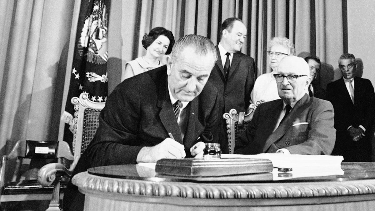  In this July 30, 1965, file photo President Lyndon B. Johnson, (left), with former Pres. Harry S. Truman at his side, uses the last of many pens to complete the signing of the Medicare Bill into law at ceremonies at the Truman Library in Independence, Missouri. John signed Medicare for people age 65 and older and Medicaid for the poor into law. His legendary arm-twisting and a Congress dominated by his fellow Democrats succeeded in creating the kind of landmark health care programs that eluded his predecessors. At rear from left are Lady Bird Johnson, Vice President Hubert Humphrey, and former first lady Bess Truman. (AP Photo, File) 
