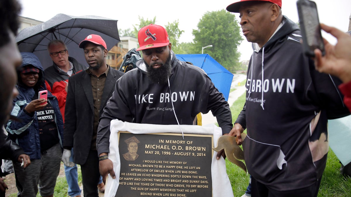  Michael Brown Sr. holds up a plaque honoring his son, Michael Brown, to show volunteers as they remove items left at a makeshift memorial last month in Ferguson, Missouri. The memorial that has marked the place where Brown was fatally shot by a police officer in August has been removed and will be replaced with the permanent plaque. (Jeff Roberson/AP Photo) 