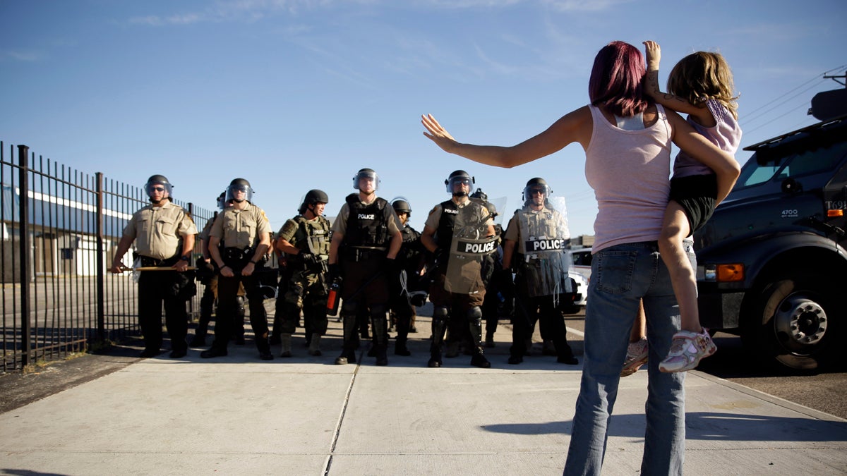  Protester Janelle Pittman holds her 6-year-old daughter, Kat, as police in riot gear stand guard in Ferguson, Mo. on Wednesday, Aug. 13, 2014. On Saturday, Aug. 9, 2014, a white police officer fatally shot Michael Brown, an unarmed black teenager, in the St. Louis suburb. (Jeff Roberson/AP Photo) 