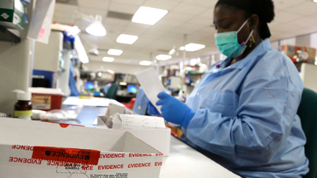 A technician handles evidence in a sexual assault case, looking down at materials on a table.