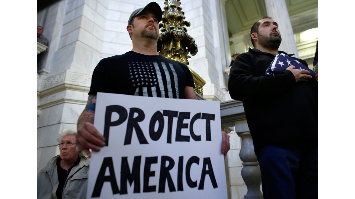  U.S. Army veteran Jim Purcell, of Burrillville, R.I., (left), displays a placard as U.S. Navy veteran Robert Martinez, (right), displays a folded American flag during a rally Thursday, Nov. 19, 2015, at the Statehouse, in Providence, R.I., held to demonstrate against allowing Syrian refugees to enter Rhode Island following the terror attacks in Paris. (Steven Senne/AP Photo) 