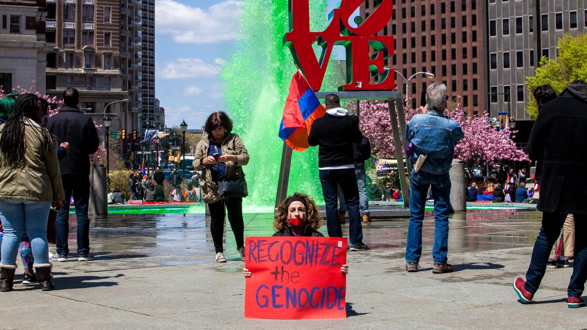 Arpy Miniasian sits in silence in front of the Love Park sign and fountain. (Brad Larrison/for NewsWorks)