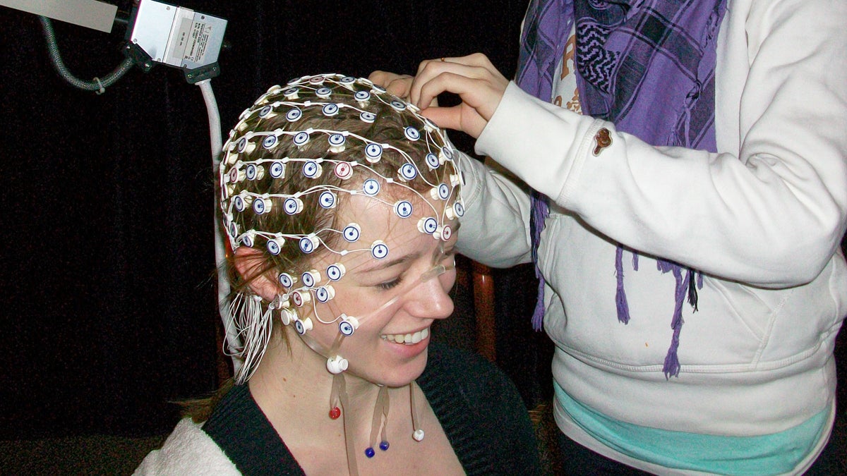 A researcher at McMaster University adjusts a net of electrodes on a participant's head. The device measures electroencephalography (EEG) responses within the brain