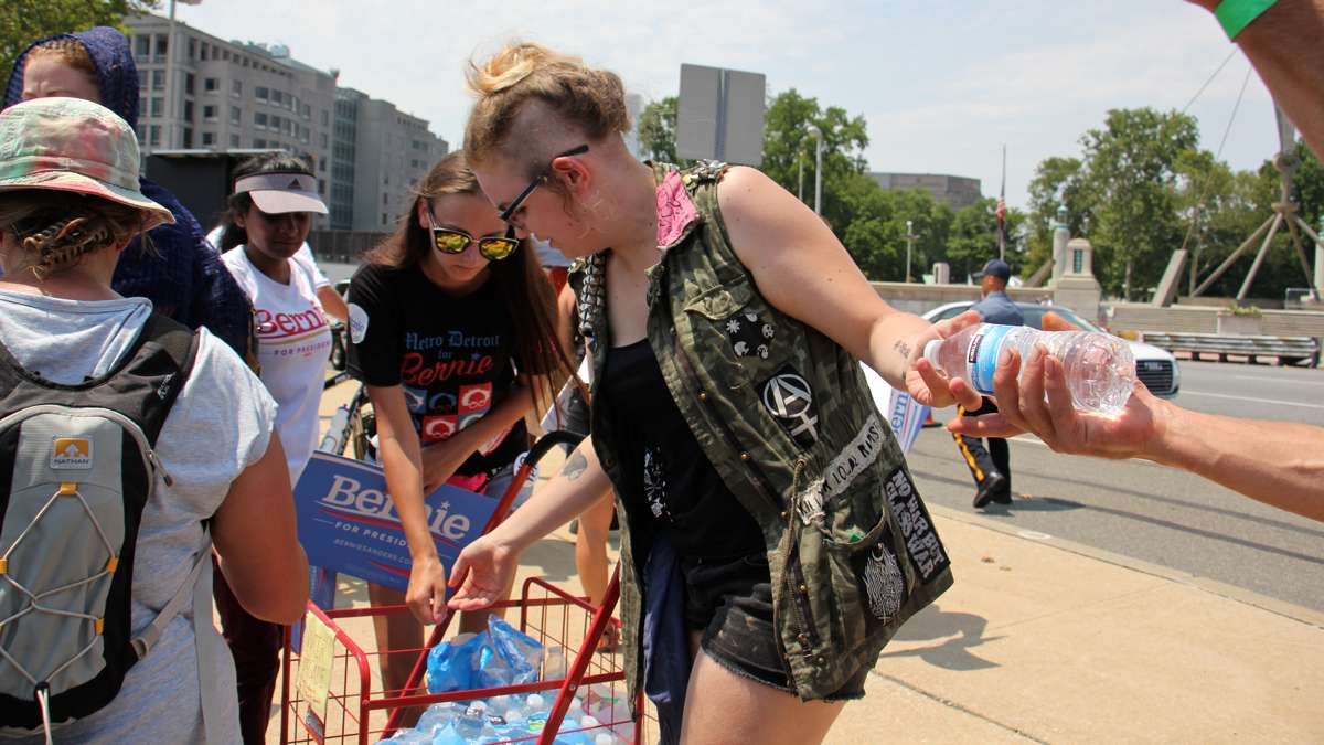 Volunteers hand out water bottles to thirsty marchers at the foot of the Ben Franklin Bridge. (Emma Lee/WHYY)