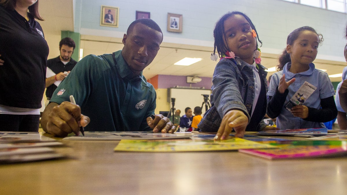 Lilyana Copeland, 7, grabs a book while Eagles conerback Brandon Boykin autographs a poster. (Brad Larrison/for NewsWorks)