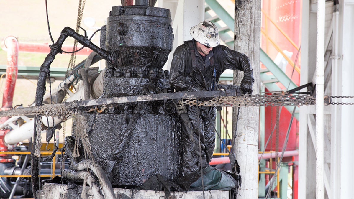 A drill worker covered in Marcellus shale, and drill cuttings seals off a well and cleans the blowout preventer at a Cabot Oil & Gas natural gas drill site in Kingsley, Pa. Washington County has nearly 1,700 Marcellus shale gas wells. (Lindsay Lazarski/WHYY)      