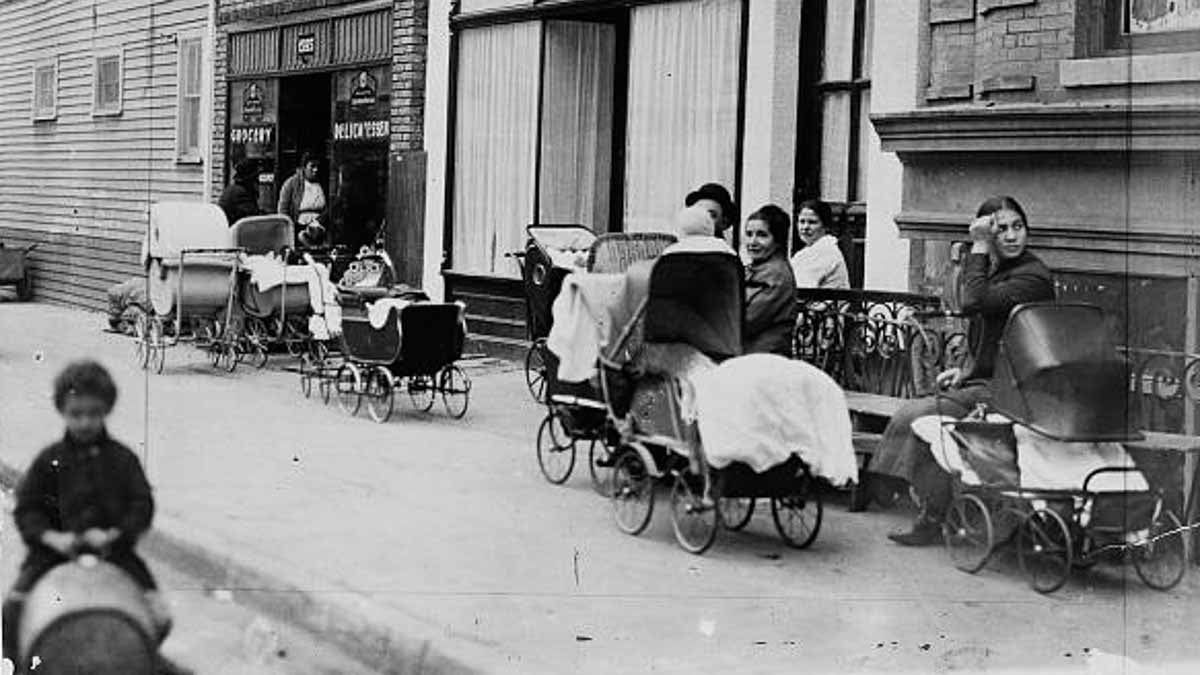 Women and men sitting with baby carriages in front of the Sanger Clinic. (<a href=