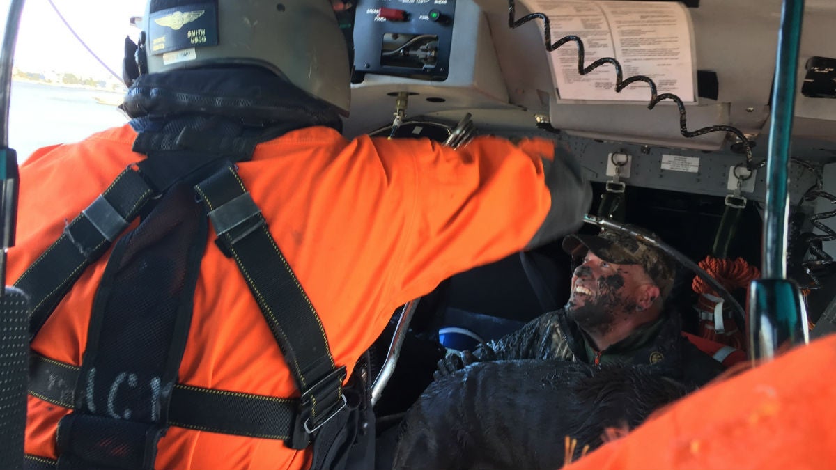 A muddy hunter smiles inside a Coast Guard helicopter after being rescued with his dog. (photo courtesy U.S. Coast Guard/ Petty Officer 1st Class Seth Johnson)