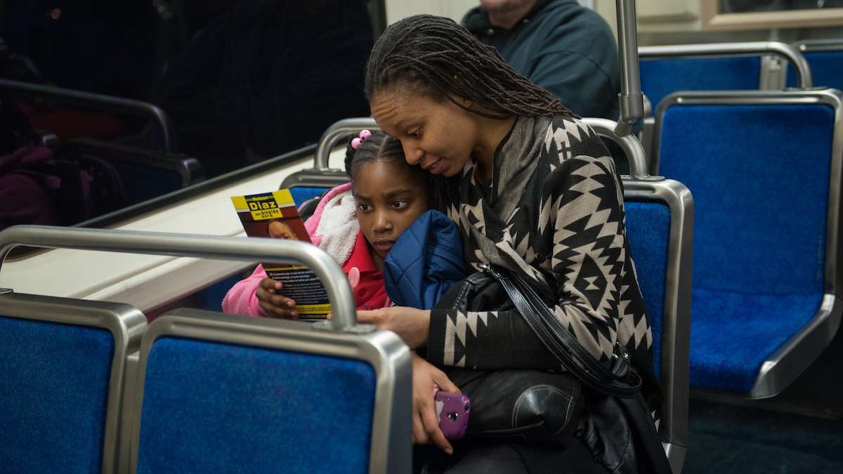  Estelle Charles and her daughter J'adore Dorvil, 8, of West Philadelphia, read a flyer that Nelson Diaz had just given them on the subway. (Tracie Van Auken/for NewsWorks) 