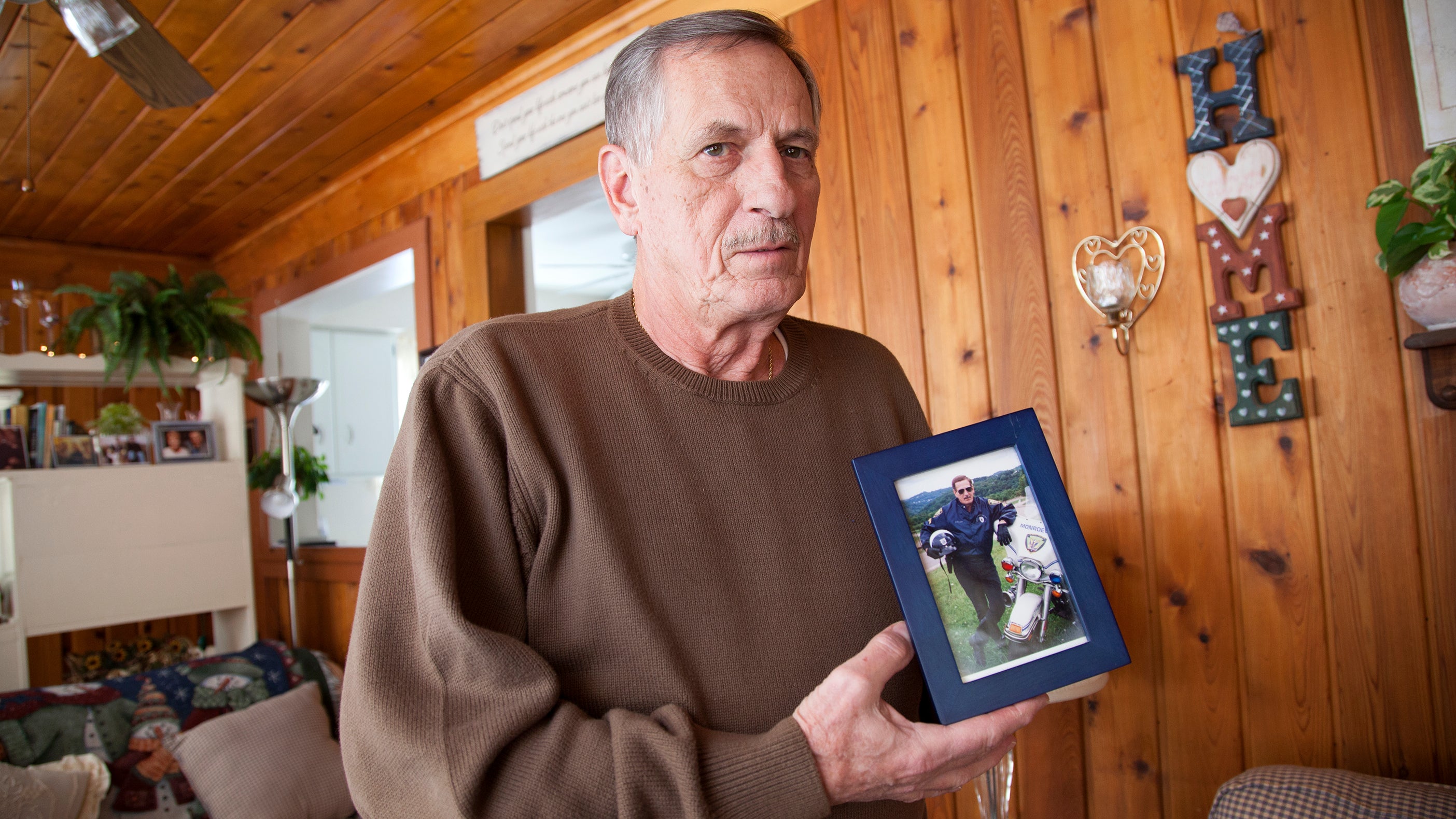  Joe Rosipal, 70, a retired Monroeville police officer, with a photograph of himself in his 40s, when he was part of the motorcycle division. (Irina Zhorov/WESA) 