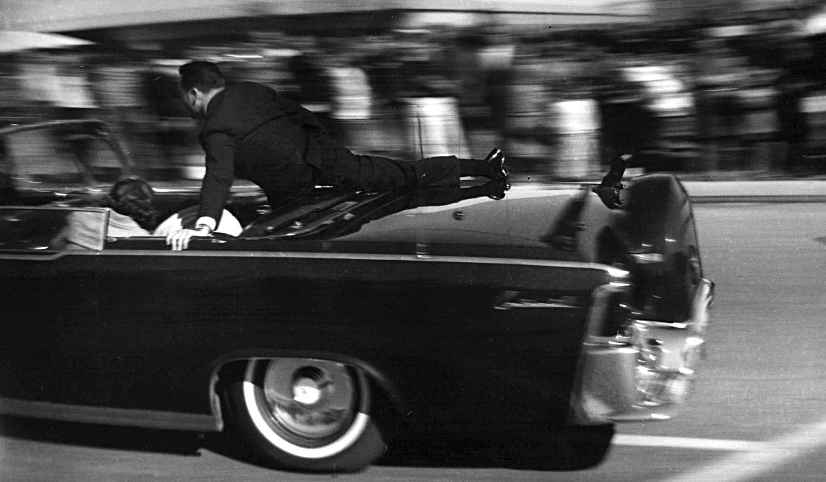  A Secret Service agent hangs on as the limousine bearing a mortally-wounded President Kennedy heads to Parkland Hospital (AP Photo/ Justin Newman). 