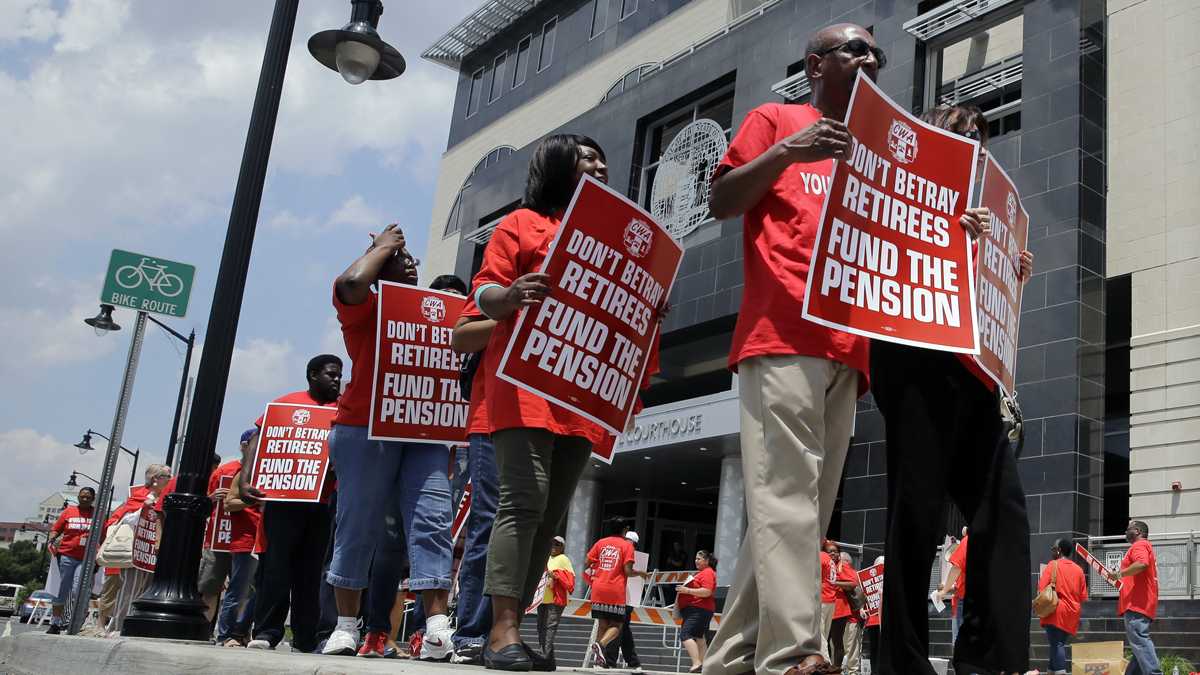  Union members carry protest signs as they march outside the Mercer County Criminal Courthouse before arguments June 25, 2014, over Gov Christie's plan to use pension payments to balance the budget. (AP Photo/Mel Evans) 