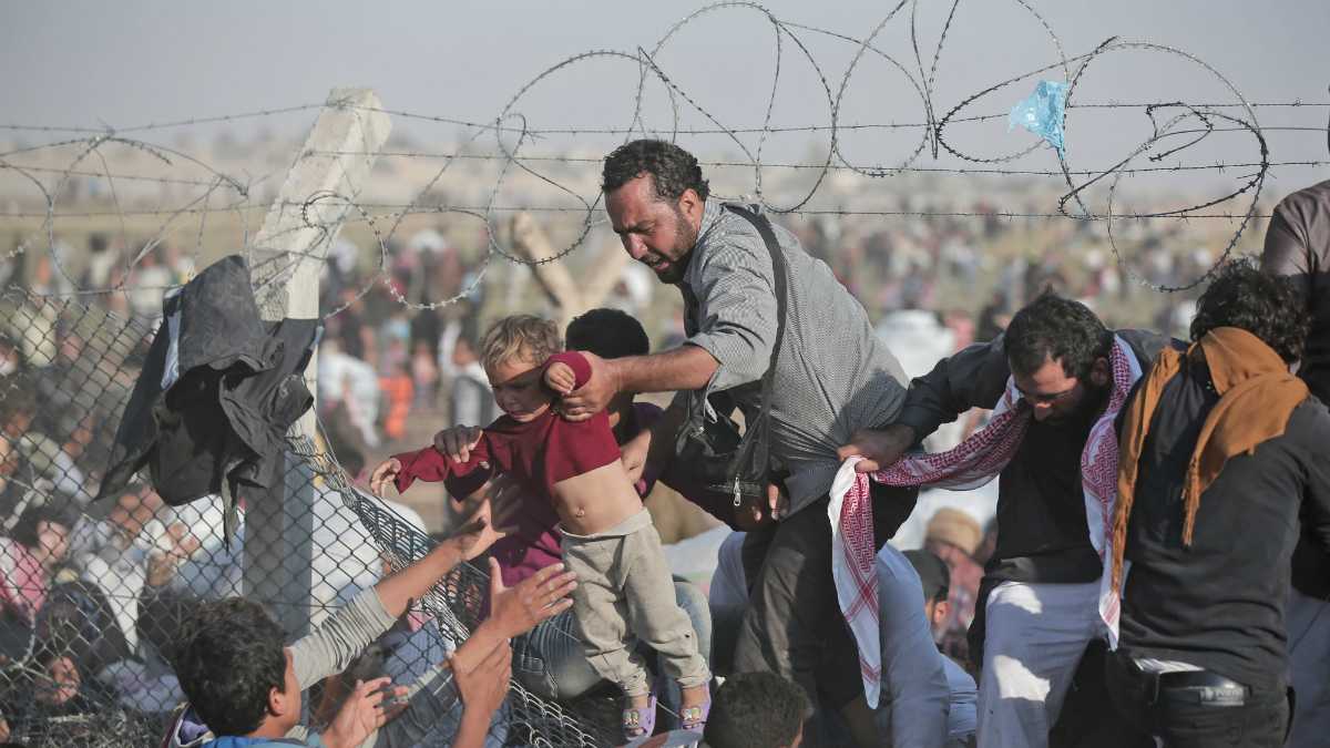  A Sunday, June 14, 2015 file photo of a Syrian refugee carrying a baby over the broken border fence into Turkey (AP Photo/Lefteris Pitarakis, File) 