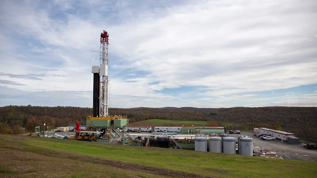 An oil rig rises up from green grass into a clouded blue sky