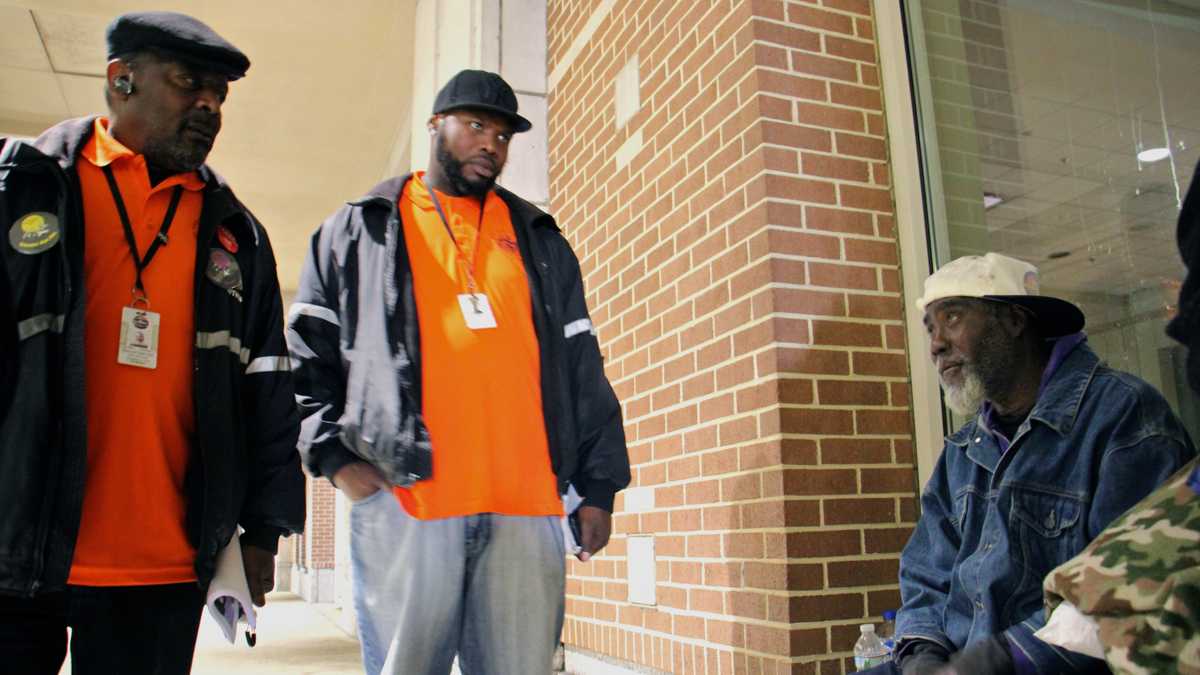 Homeless outreach workers talk with a man who has camped out on 12th Street in the shelter of the Pennsylvania Convention Center. (Emma Lee/WHYY)
