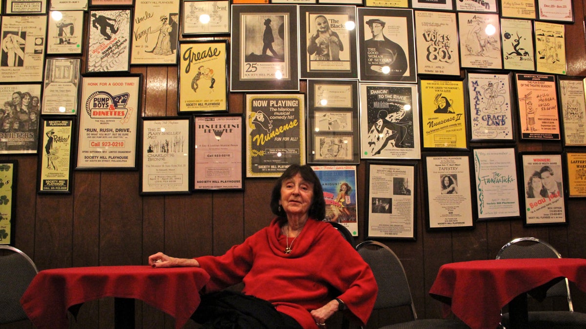 Deen Kogan, who opened the Society Hill Playhouse in 1960 with her husband, Jay, sits beneath the posters that adorn the lobby. (Emma Lee/WHYY)