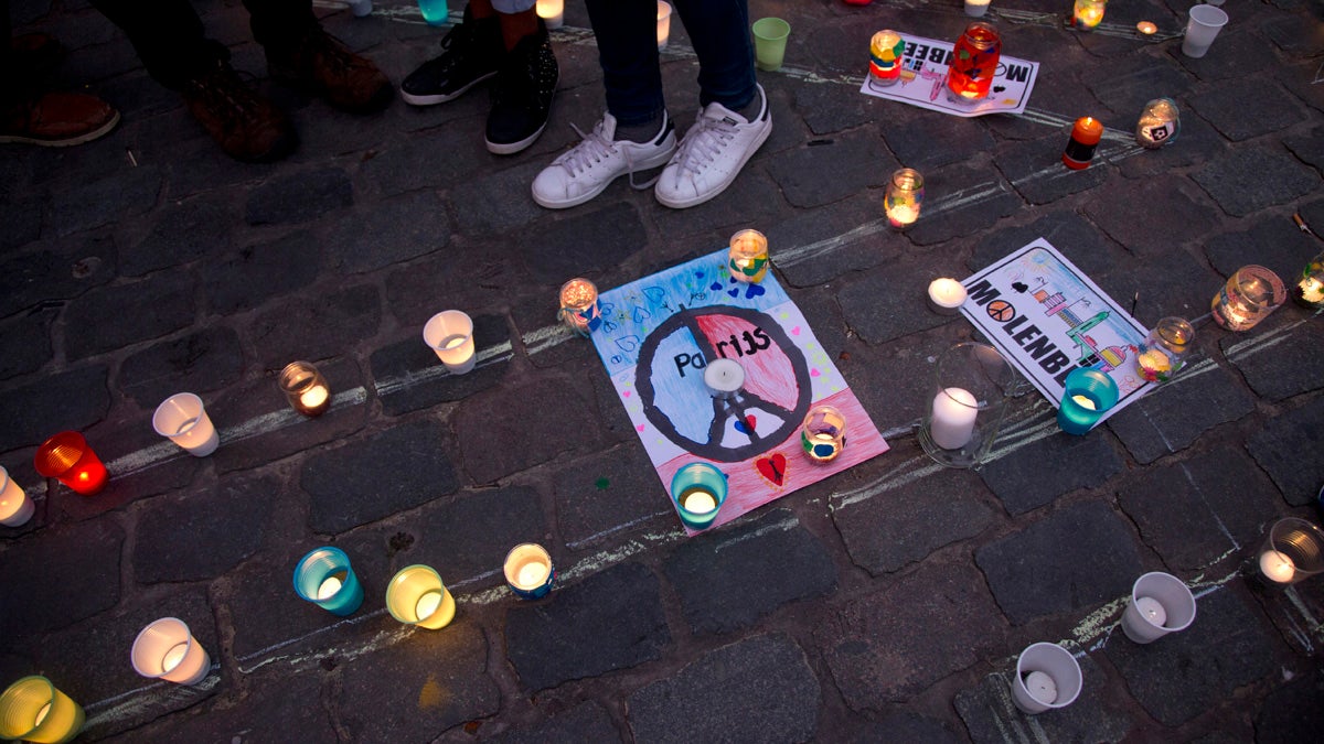 People stand next to candles and banners during a candlelight vigil for the Paris attacks in the town square of Molenbeek