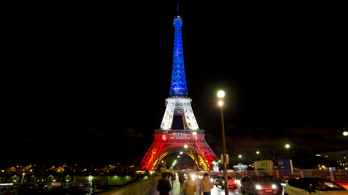 People walk towards the illuminated Eiffel Tower in the French national colors of red