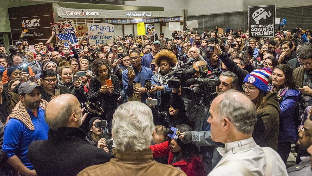 Media and protesters crowd around, (from left), Governor Tom Wolf, Representative Bob Brady, and Senator Bob Casey as they speak about their opposition and the developing situation regarding President Donald Trump’s executive order on immigration at the Philadelphia International Airport. (Branden Eastwood for NewsWorks)