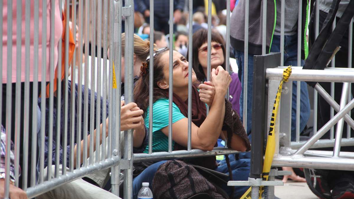  A woman clings to the bars of a barricade as she watches Pope Francis on a jumbotron near City Hall. (Emma Lee/WHYY) 