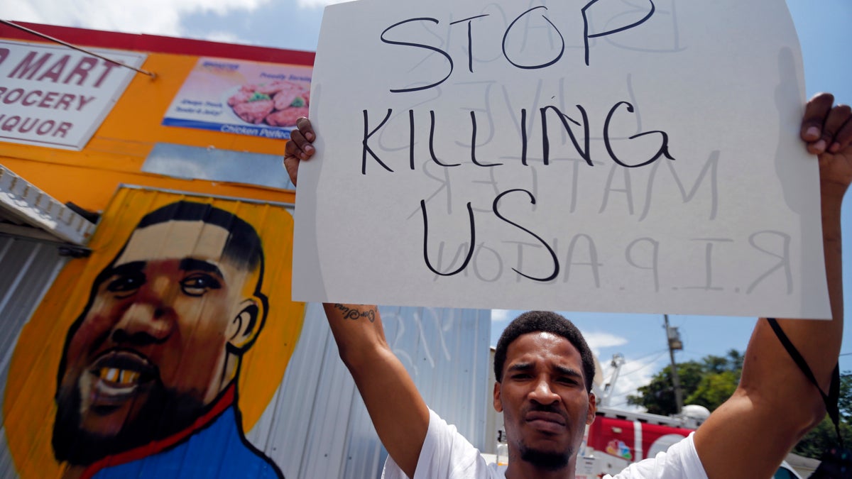 A man holds a sign in front of a mural of Alton Sterling while attorneys