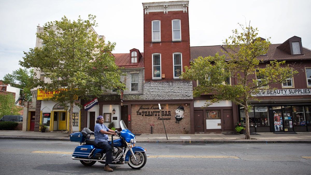 A motorcyclist rides by shops and restaurants on Penn Street including Jimmie Kramer’s Peanut Bar in downtown Reading.  (Lindsay Lazarski/WHYY) 