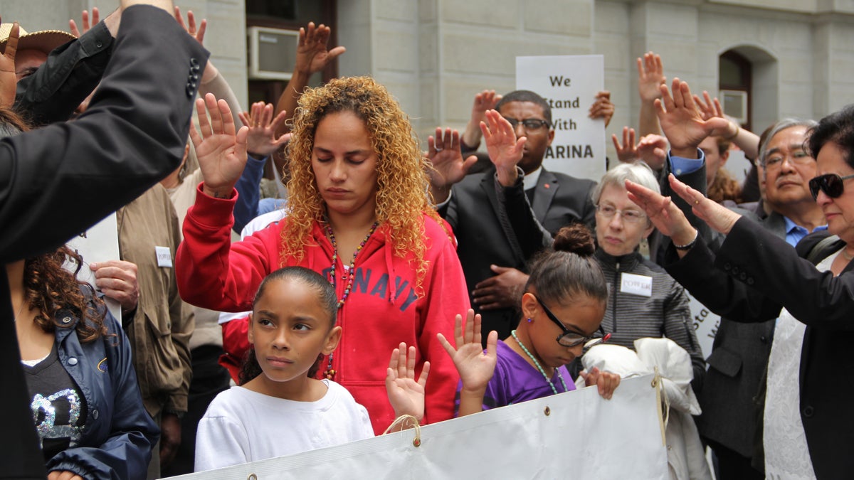  Members of POWER hold their hands over Sarina Santos and her family in a gesture of protection and prayer. The former baggage handler lost her job at Philadelphia Airport after speaking out about workers' rights. (Emma Lee/WHYY) 