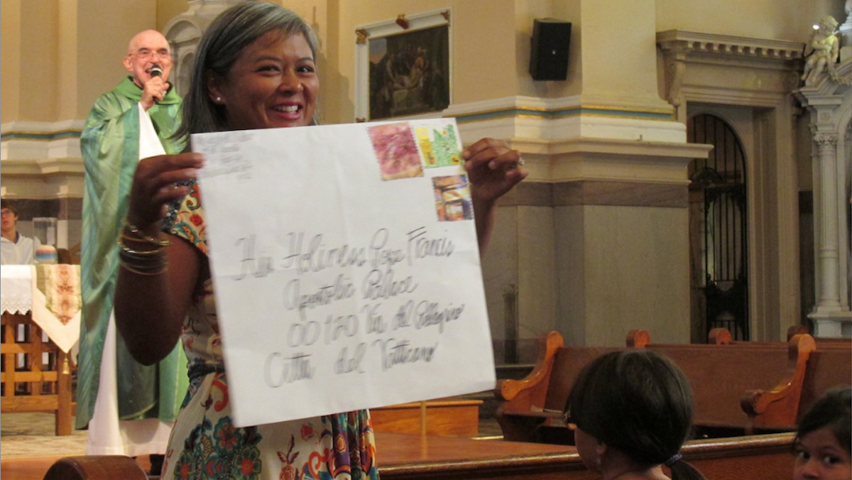  With Father Sy Paterka in the background, Maria Beatty holds an oversized envelope in which letters inviting Pope Francis to Germantown will be mailed. (Photo courtesy of St. Vincent de Paul Parish) 