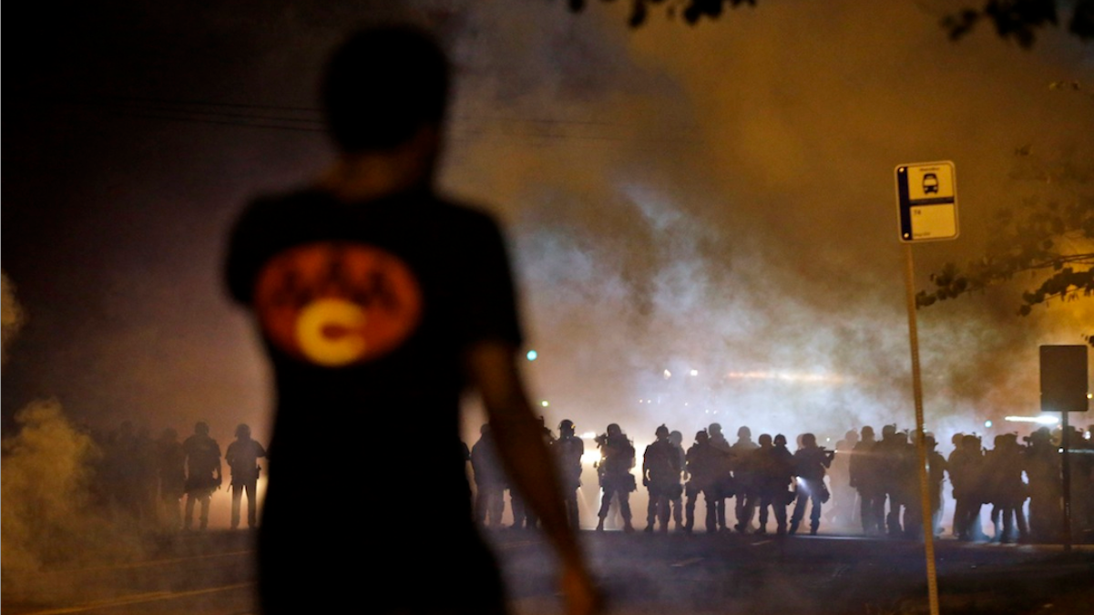  A man watches as police walk through a cloud of smoke during a clash with protesters in Ferguson, Mo. (AP Photo/Jeff Roberson) 